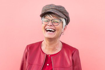 Happy senior woman having fun outdoor - Trendy mature person laughing and enjoying retired time - Elderly people lifestyle and mother's day concept - Coral Background - Powered by Adobe