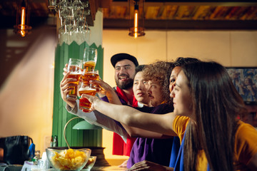 Sport fans cheering at bar, pub and drinking beer while championship, competition is going. Multiethnic group of friends excited watching translation. Human emotions, expression, supporting concept.