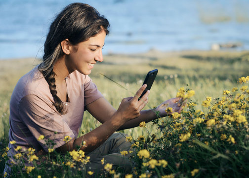 Beautiful Woman Taking A Picture With Her Cell Phone To Some Wild Flowers