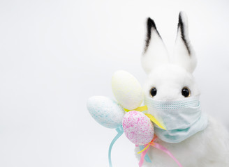 Easter Bunny in a facial medical mask with a bouquet of colorful eggs. The concept of Easter and quarantine during coronavirus. Like a postcard wishing you well