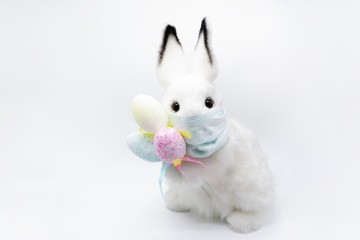Easter Bunny in a facial medical mask with a bouquet of colorful eggs. The concept of Easter and quarantine during coronavirus. Like a postcard wishing you well