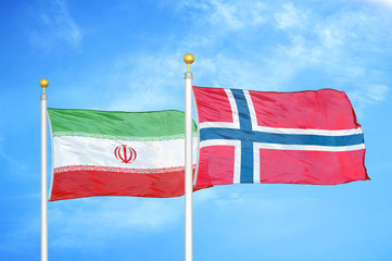Iran and Norway two flags on flagpoles and blue cloudy sky