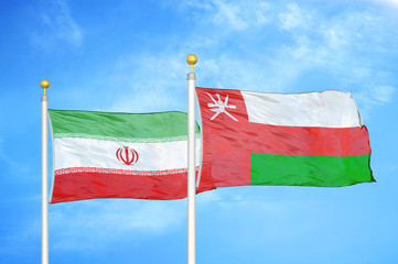 Iran and Oman two flags on flagpoles and blue cloudy sky