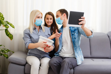Obraz premium Family couple in medical face masks lying on a bed with a laptop. Concept of watching video, working together and quarantine during a COVID-19 coronavirus epidemic