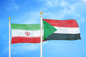 Iran and Sudan two flags on flagpoles and blue cloudy sky