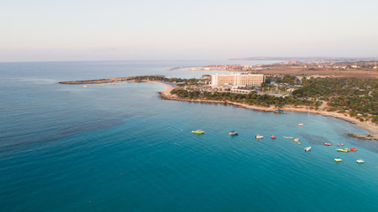 Naklejka na ściany i meble Aerial bird's eye view of Landa beach, Ayia Napa, Famagusta, Cyprus. Landmark tourist attraction golden sand bay at sunrise with boats anchored between Makronissos and nissi in Agia Napa, from above. 