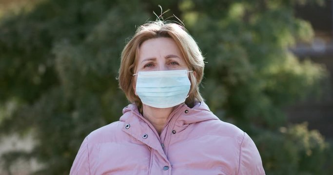 Senior Woman Takes on Medical Mask. Breathes deeply and looking at camera on Green Background. Health care and medical concept