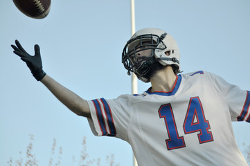 Player jumping to catch American football ball with the sky as background