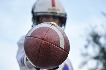 Player holding an American football ball in front of his face. Man hiding behind a ball. Player out of focus and a ball in the foreground