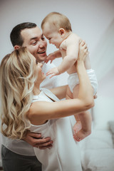 Smiling young couple playing with their beloved newborn baby girl on the bed