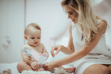 Baby girl playing with her beloved young mother on the bed