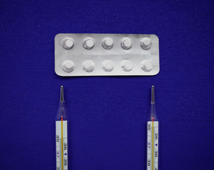 Top view on two thermometers and white pills on a blue background. Virus pandemic
