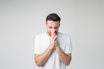 Young man isolated over background. Sick person with nose running. Using white napkin. Coronavirus danger. Ill male person inside studio room.