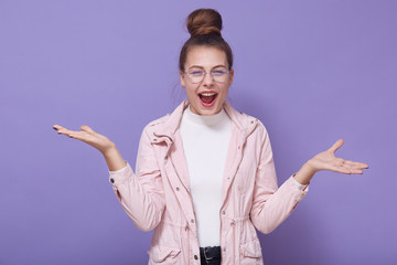 Horizontal shot of exited caucasian young woman spreads hands, wearing fashion pastel jacket and...