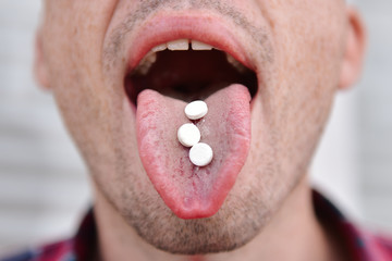Cut view and close up of man with opened mouth with three white pills on tongue. Drugs addicted or...