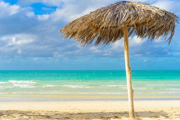 Fototapeta na wymiar Caribbean landscape with beach umbrella. Vacation in Cuba. Palm leaf umbrella on the Cuban beach. Rest from all worries. Paradise. Travel to Cuba. White sand and emerald water of the Caribbean sea.