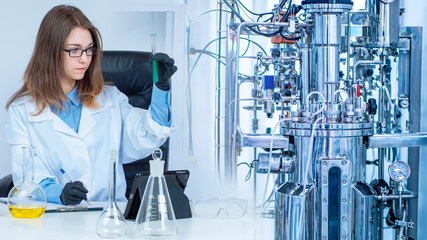 Girl with test tubes on the background of a laboratory bioreactor. Bioengineer in the workplace....