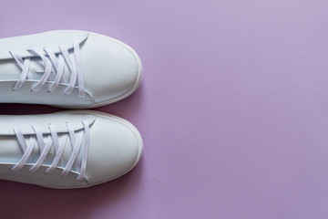 A pair of white sneakers on purple background. Copy space.