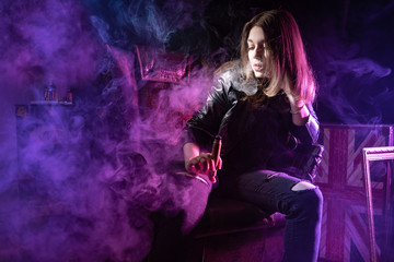 Girl posing with an electronic cigarette. Smoking. A student holds a vape device. Dark. Woman in a...