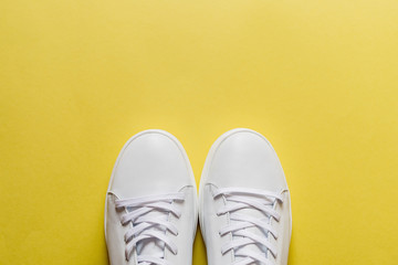 A pair of white leather sneakers on yellow background. Copy space.