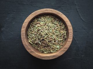 Dried rosemary in wooden bowl on dark vintage background. Overhead shot.