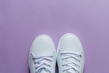 A pair of white sneakers on purple background. Copy space.