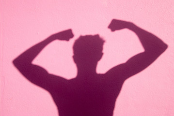 Shadow of unrecognizable thin man flexing his muscles outdoors against a bright pink wall