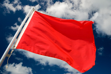 Fototapeta na wymiar Bright red warning flag waving outdoors under sunny blue sky
