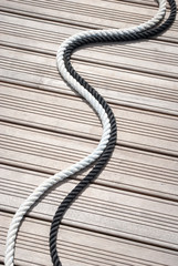 Black and white nautical ropes curving together outdoors on a wooden background