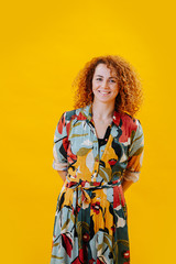 Portrait of a cheerful red-haired girl in a colored jumpsuit, against the background of a yellow wall