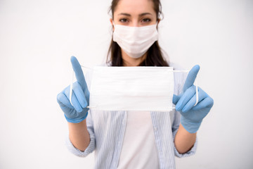 A Girl in medical gloves and in protective mask holds a medical mask in her hands on a white background. Respiratory disease. Covid-19