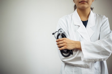 Closeup of a woman doctor wearing white medical gown and blue gloves, stethoscope. Female nurse holding a stethoscope in her hand, hands crossed. Coronavirus, covid-19 and sickness prevention concept.