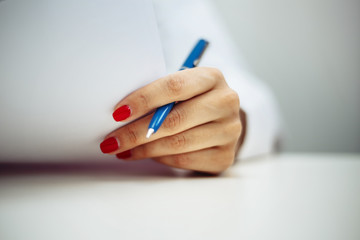 Closeup of a female doctor hands with a blue pen making notes and filling in diagnosis of patient on a paper. Coronavirus test and prevention concept. Epidemic pandemia of covid-19 nCov2019.