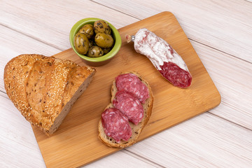 Sandwich of dried sausages, olives and a loaf of whole grain bread on a wooden board. The concept of simple affordable food.