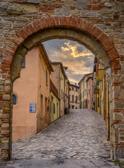 Empty Italian medieval street covered with cobblestone viewed from the city gate in San Leo during sunset