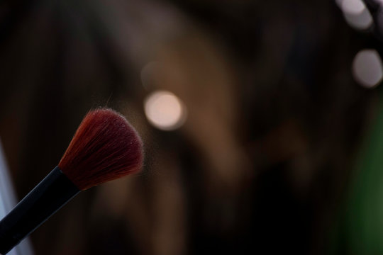 Makeup brush with red bristles having leftover extra loose wheatish powder held against soft light