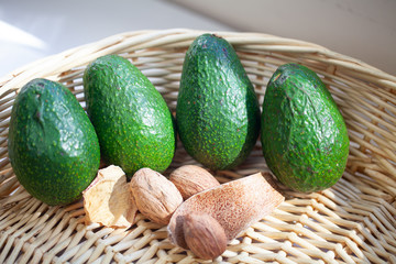 Four green avocados lining up in rattan basket, nuts and dried wood chips in the front