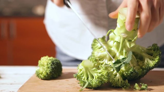Female using a sharp knife for chopping a broccoli Cabbage on wooden cutting board ah home kitchen. Food preparation concept footage.