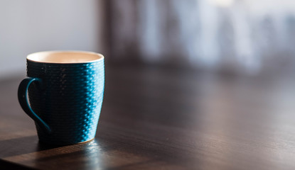Cup. Blue cup standing on a wooden table. Blurred background. The sun is shining on the cup.