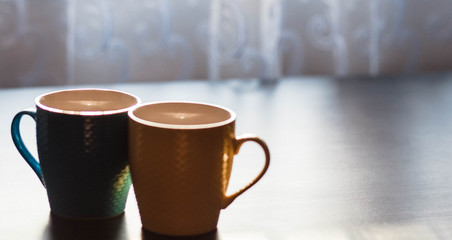 Cups. Colored cup standing on wooden table. Blurred background. The sun is shining on the cup.