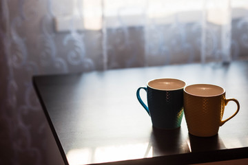 Cups. Colored cup standing on wooden table. Blurred background. The sun is shining on the cup.