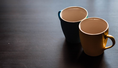Cups. Colored cup standing on wooden table. Blurred background. The sun is shining on the cup.