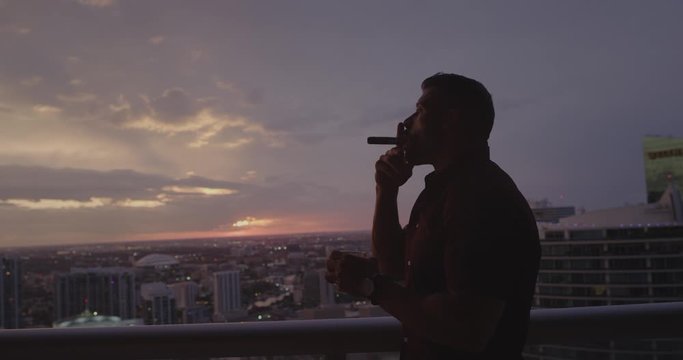 Man smoking cigar on balcony at sunset