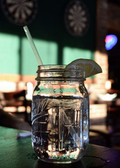 Glass with soda, ice, a lemon wedge and a straw with a target background.