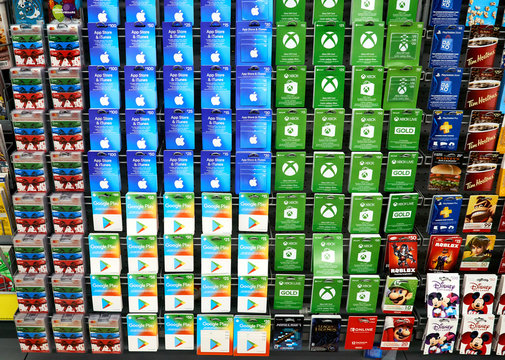 A Background Image Of A Stand With Gift Cards Of Apple Store, McDonalds, Xbox, Nintendo, ITunes, Visa, Playstation, Google Play, Minecraft