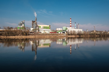 Fototapeta premium pipes of woodworking enterprise plant sawmill near river. Air pollution concept. Industrial landscape environmental pollution waste of thermal power plant