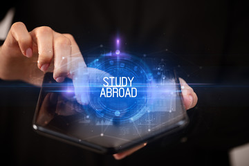 Young man holding a foldable smartphone with STUDY ABROAD inscription, educational concept