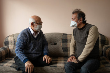 An elderly and a senior man wearing masks chatting about covid19