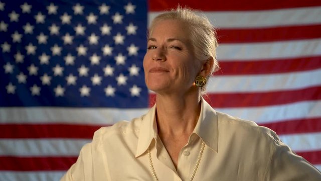Professional looking mature woman smiling and showing us her arm muscles in front of an American flag.