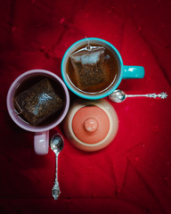 Dos tazas de té y azucarera con cucharas de plata sobre mantel rojo